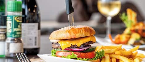 A plate with a burger, fries, and a glass of white wine on a table.