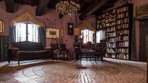 Una habitación con piso de ladrillo, un sofá de madera, una araña, una estantería y una ventana con cortinas.
