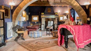 Una habitación con un arco de piedra, una chimenea, una mesa cubierta con mantel rojo y una alfombra estampada.