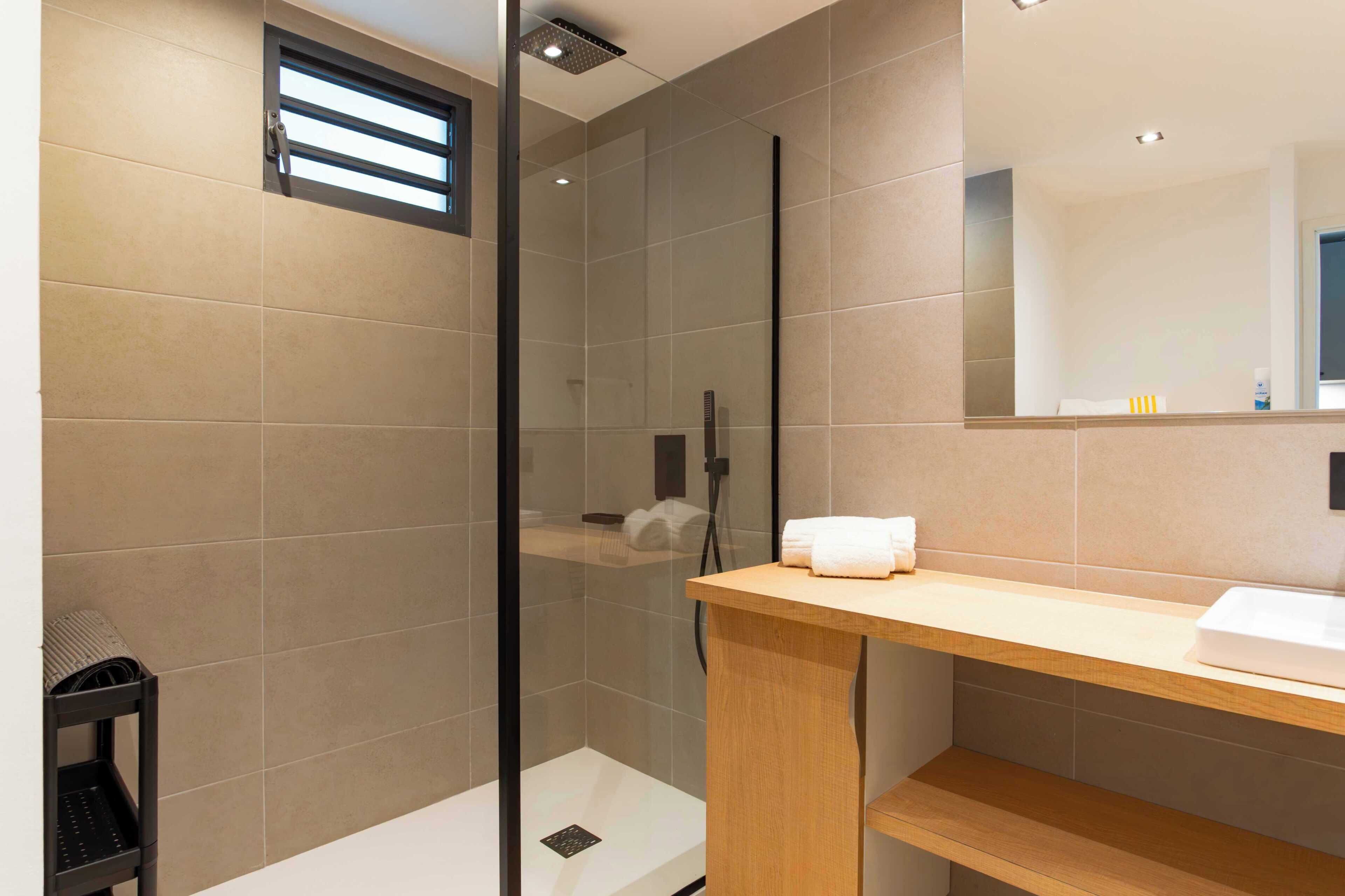 Un baño moderno con cabina de ducha de vidrio, tocador de madera y espejo.