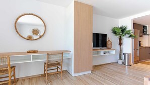 A modern living room with a wooden dining table, two wicker chairs, a large mirror, a flat-screen TV, a small plant, and a kitchen area with a refrigerator and microwave. - Beautiful studio on the beachfront Baie Orientale (Saint-Martin)