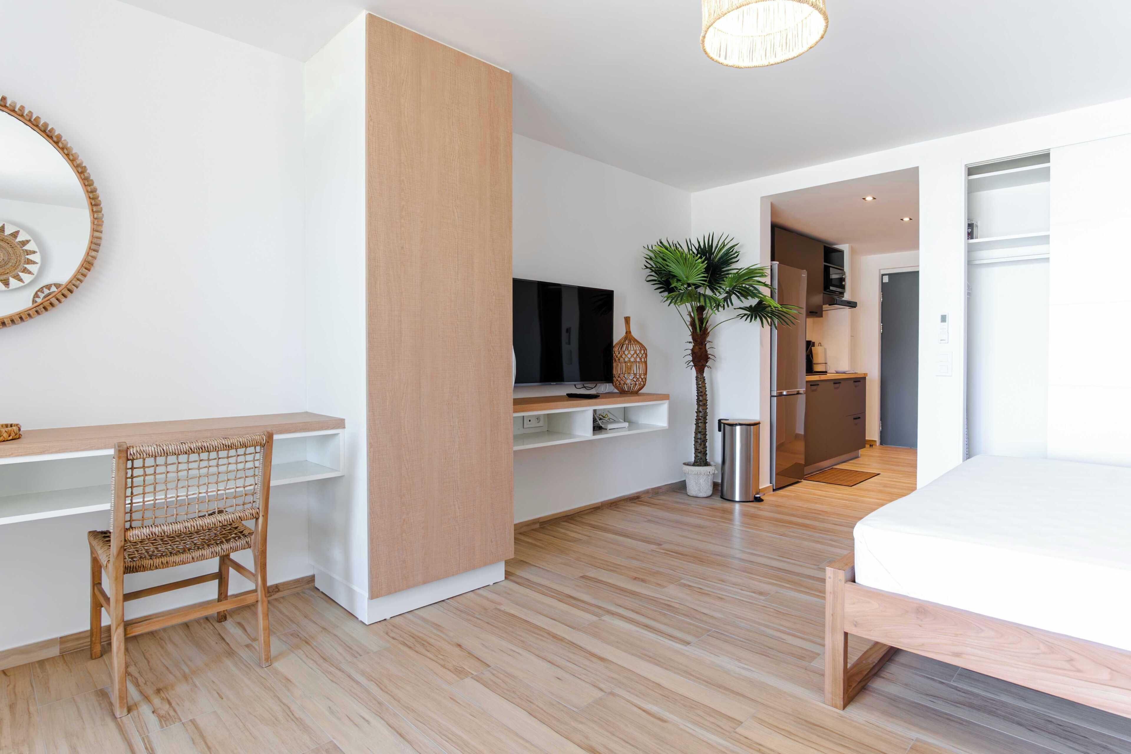 Una camera d'albergo moderna con pavimento in legno, un letto, una scrivania con sedia, una televisione, una pianta e un angolo cottura.