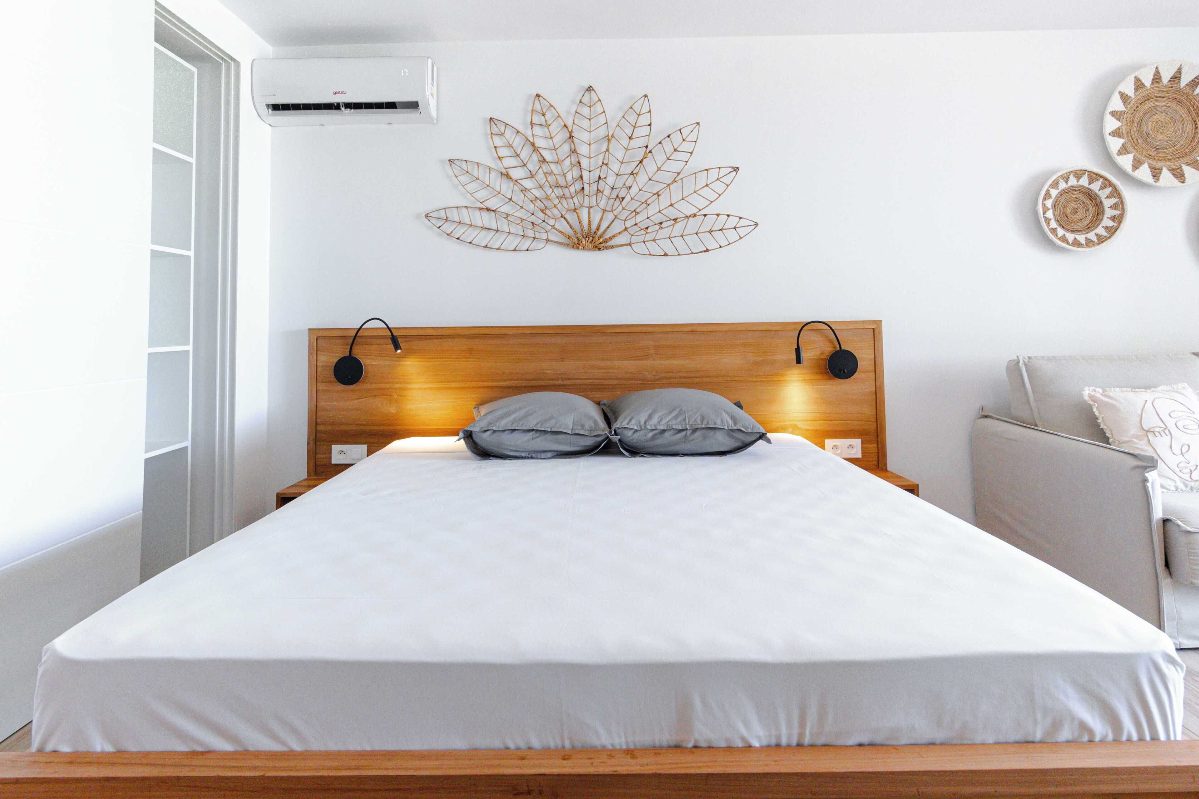 A bedroom with a wooden headboard, two bedside lamps, a bed with white bedding, and a wall-mounted decorative leaf.