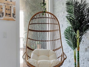 Curl up in your own cozy hanging chair, surrounded by bright white brick and tropical greenery—a perfect nook for morning coffee or afternoon relaxation.