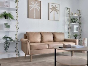 Ein beiges Sofa mit zwei Kissen, ein runder Couchtisch und eine weiße Regaleinrichtung mit Pflanzen und gerahmten Kunstwerken.