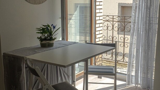 Een balkon met een tafel en stoelen, een bloempot en een sierhek van metaal.