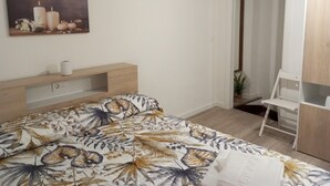 Een slaapkamer met een bed, een nachtkastje, een schilderij, een deur met een vluchtbord en een witte stoel.