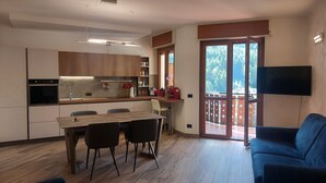 Eine moderne Küche mit Essbereich, ein Balkon mit Fernseher und ein blaues Sofa.