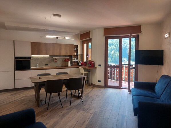 Una cocina moderna con comedor, un balcón con televisor y un sofá azul.