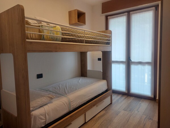 Una cama individual en literas con un cajón para guardar objetos, una mesita de noche y una ventana con persianas.