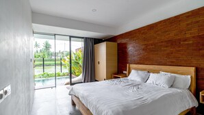 Un dormitorio moderno con una cama grande, cabecera de madera, mesita de noche y puerta corredera de vidrio que da a un balcón con vistas al verdor.