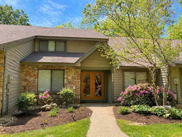 A two-story house with a stone facade, a front door with glass panels, and a well-maintained garden with flowering plants.