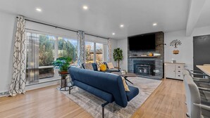A modern living room with a blue sofa, a fireplace, a TV, and a dining area with a table and chairs.
