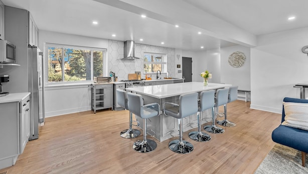 A modern kitchen with a central island, bar stools, and a dining area with a large table.