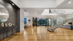 Un ampio soggiorno moderno con pavimento in legno, una scala in vetro e vista sull'esterno.