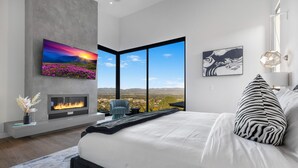 Una camera da letto moderna con un letto grande, un camino, una TV e vista sulla città.