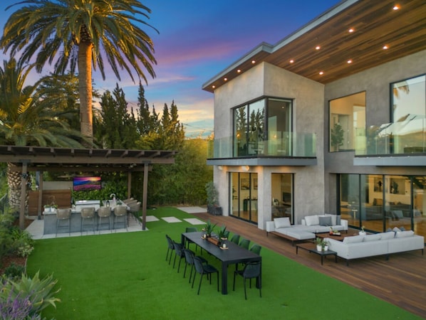 A modern two-story house with a covered outdoor area, a patio, and a well-maintained lawn.