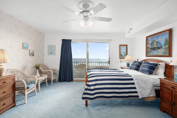 Un dormitorio con cama, silla, cómoda, ventilador de techo y vista al océano.