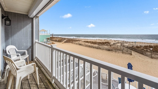 A balcony with a view of the beach, white plastic chairs, and a lifeguard tower. - Midtown 4 bedroom oceanfront townhome, steps from the beach (Ocean City)