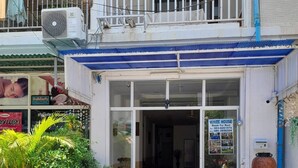 A two-story building with a blue roof and white walls. There is a sign for "White House" indicating it is for rent. The entrance has a glass door, and there are potted plants in front. - White House by Sorot (Pattaya)