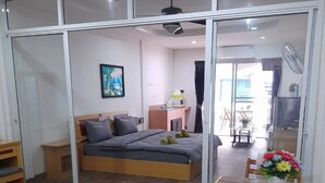 A bedroom with a bed, a desk, and a chair. There is a window and a door. - White House by Sorot (Pattaya)