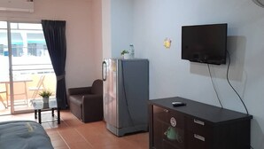 A hotel room with a bed, a desk, a refrigerator, a television, and a ceiling fan. - White House by Sorot (Pattaya)