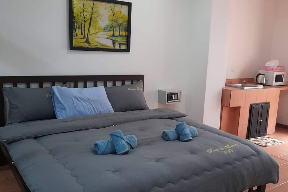 A bedroom with a bed, a painting on the wall, and a kitchenette area.