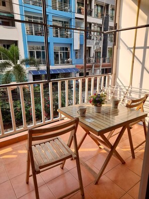 A balcony with a glass table and wooden chairs, overlooking a residential area with blue and white buildings. - White House by Sorot (Pattaya)