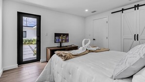 Una habitación de hotel moderna con cama, televisión, escritorio y puerta corredera al exterior.