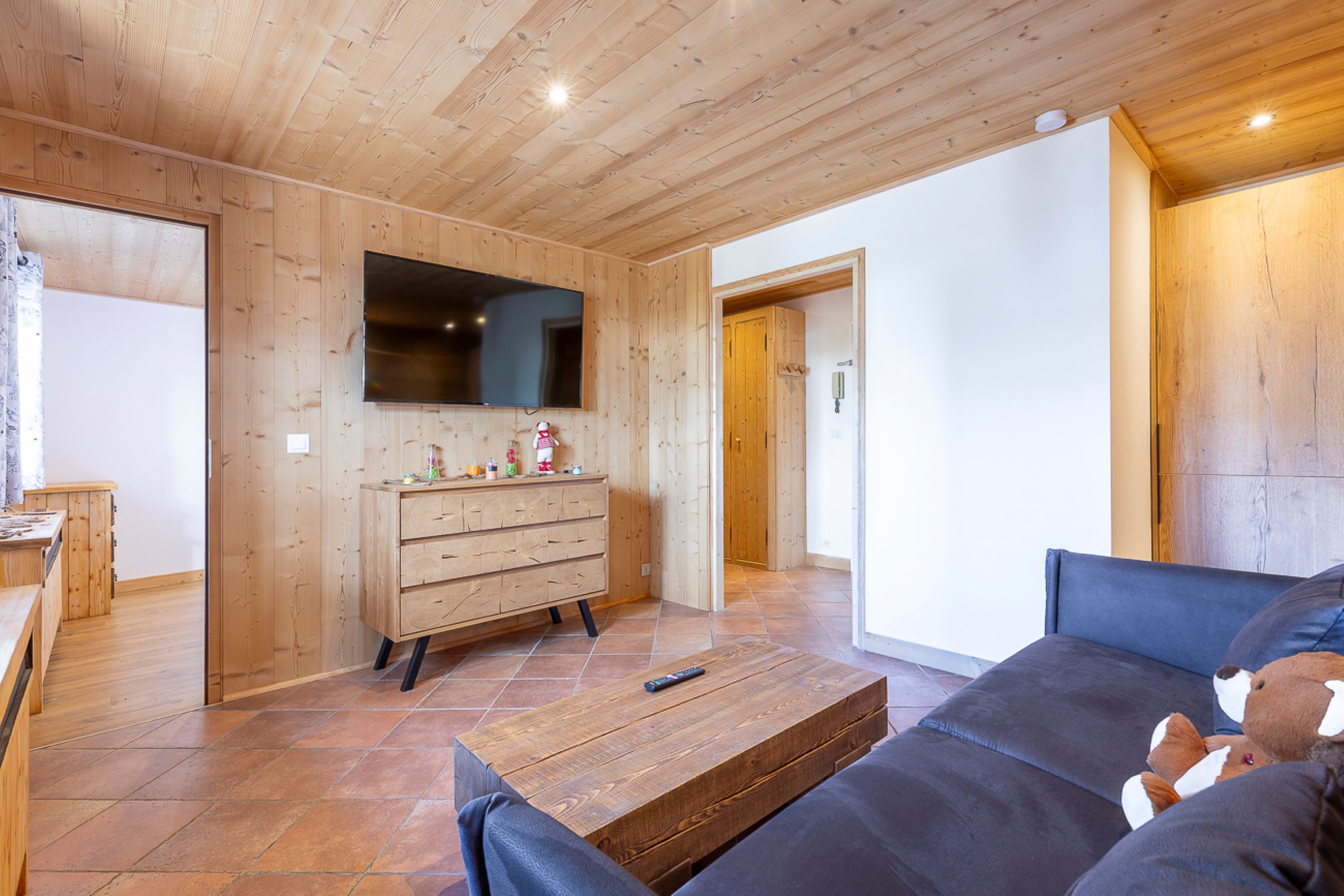 A wooden-paneled room with a sofa, a wooden dresser, and a flat-screen TV mounted on the wall.