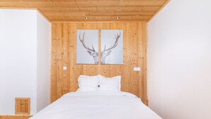 Een slaapkamer met een houten plafond, een bed met wit beddengoed en twee schilderijen van hertenhoorns aan de muur.