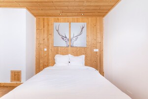 Une chambre avec un plafond en bois, un lit recouvert de linge de lit blanc et deux tableaux représentant des bois de cerf accrochés au mur.