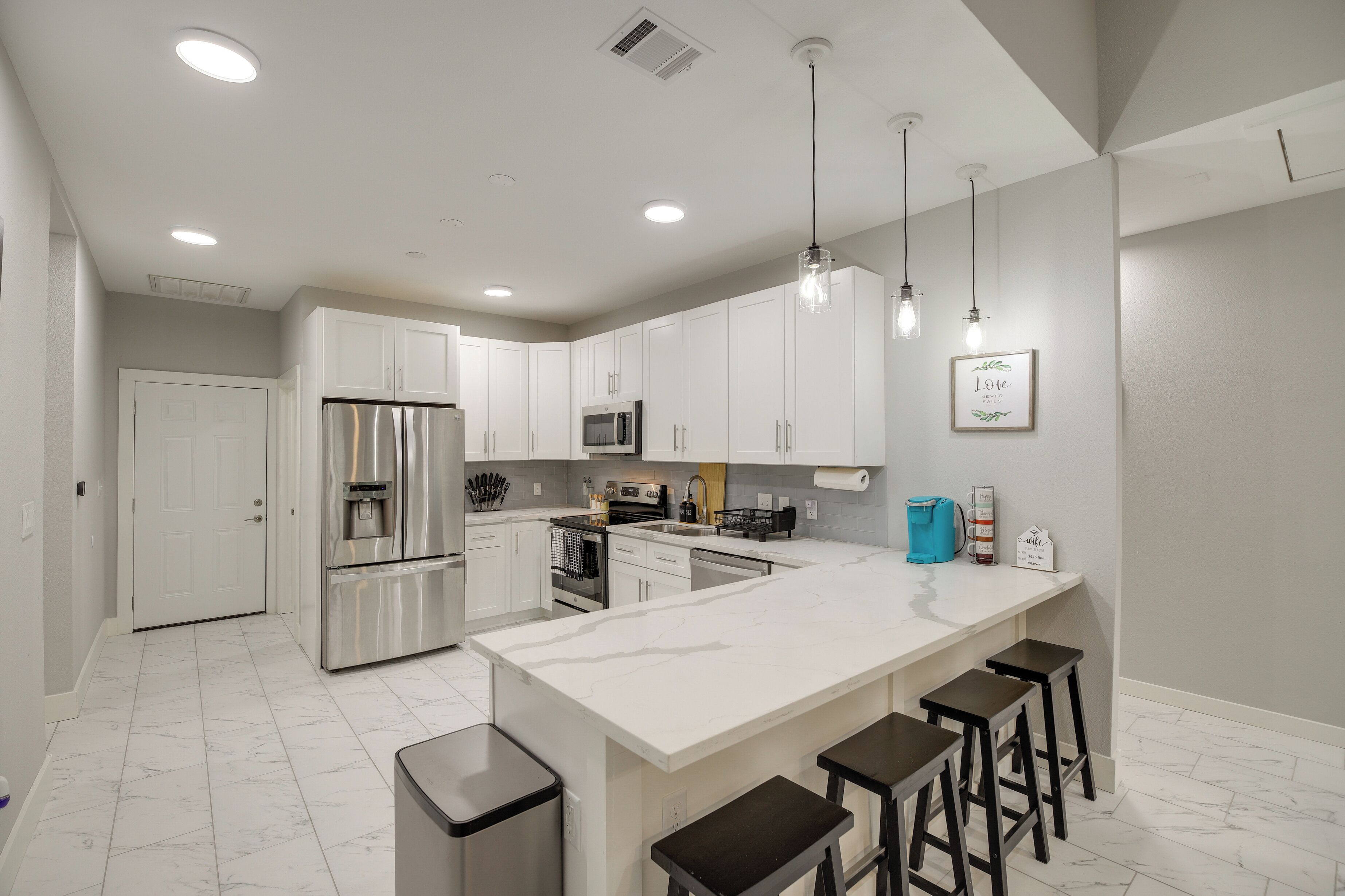 A modern kitchen with white cabinets, stainless steel appliances, and a marble island with bar stools.