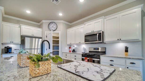 Una cocina moderna con armarios blancos, electrodomésticos de acero inoxidable, una encimera de mármol y un reloj en la pared.