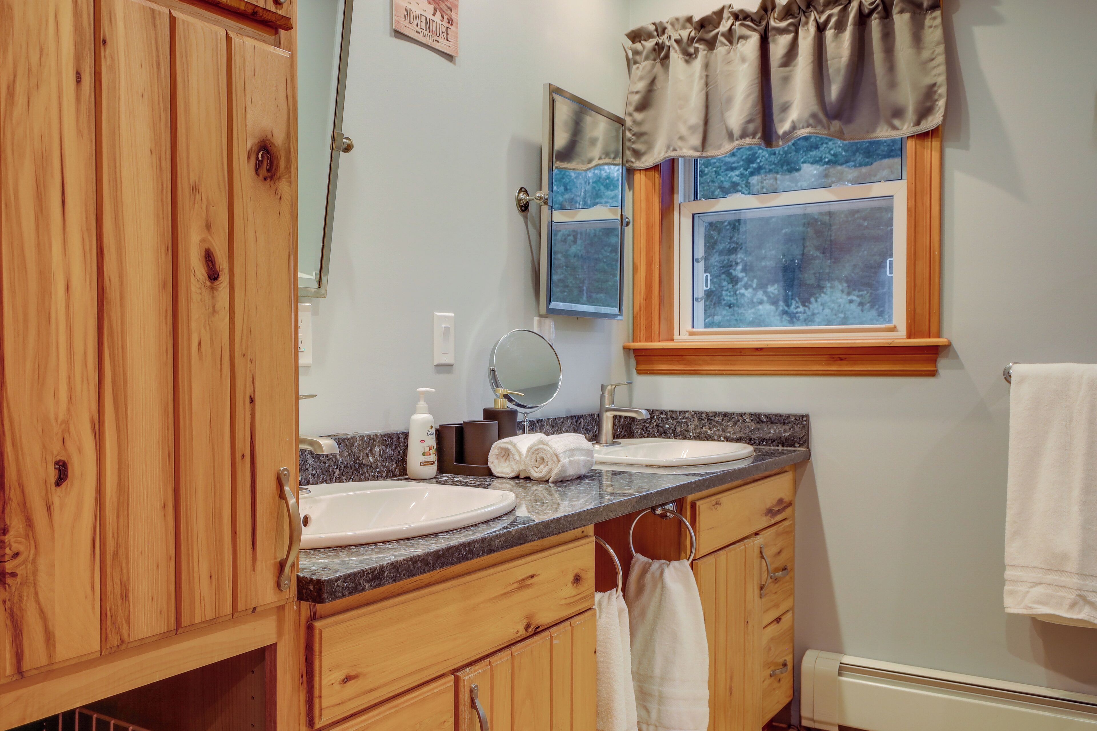 A bathroom with wooden cabinets, a sink, a mirror, and a window with a view of trees.