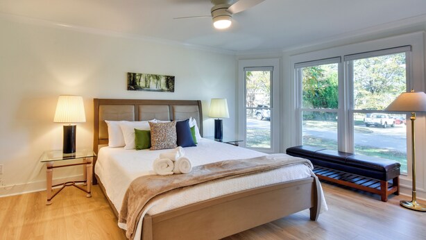 A bedroom with a large bed, two bedside tables, a ceiling fan, and a window with a view of the outside. - Tranquil Travelers Rest Home w/ Fire Pit! (Travelers Rest)