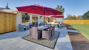Een terras met een tafel en stoelen met een glazen blad, een rode parasol en een houten schutting.