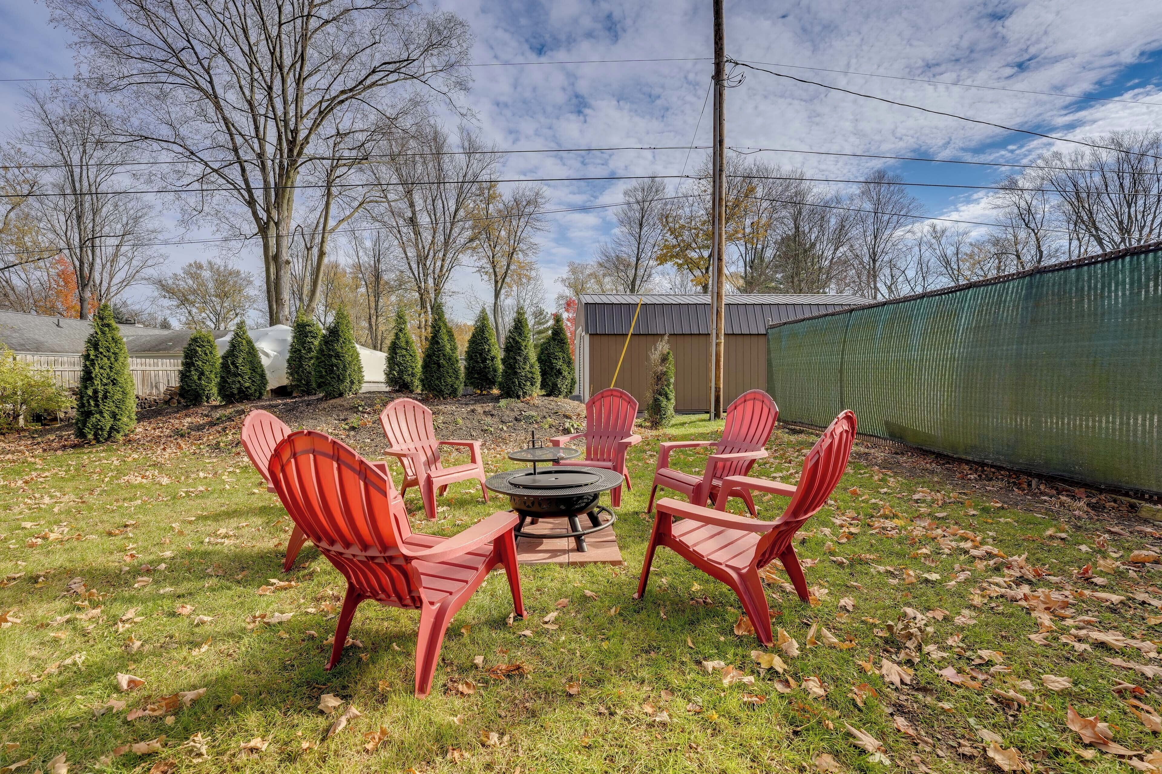 Un jardin avec un foyer, des chaises Adirondack rouges et une clôture verte.