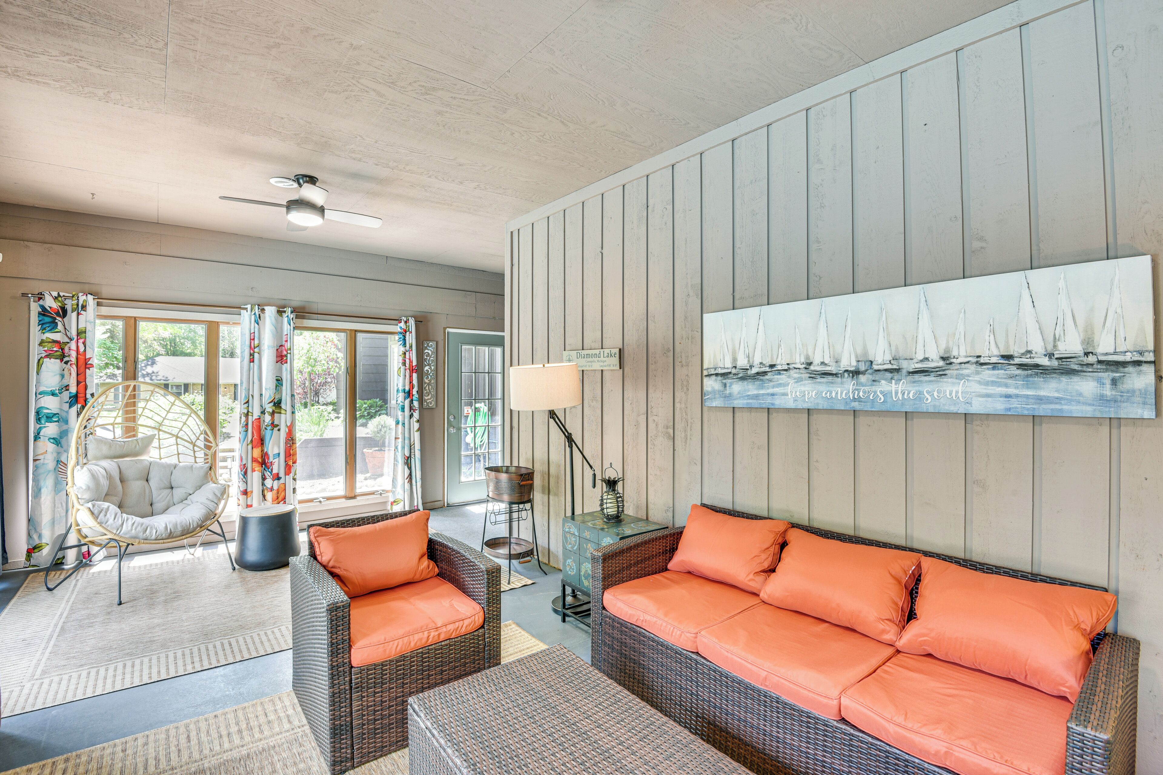 A cozy living room with wicker furniture, a large painting of sailboats, and a sign reading "Diamond Lake."