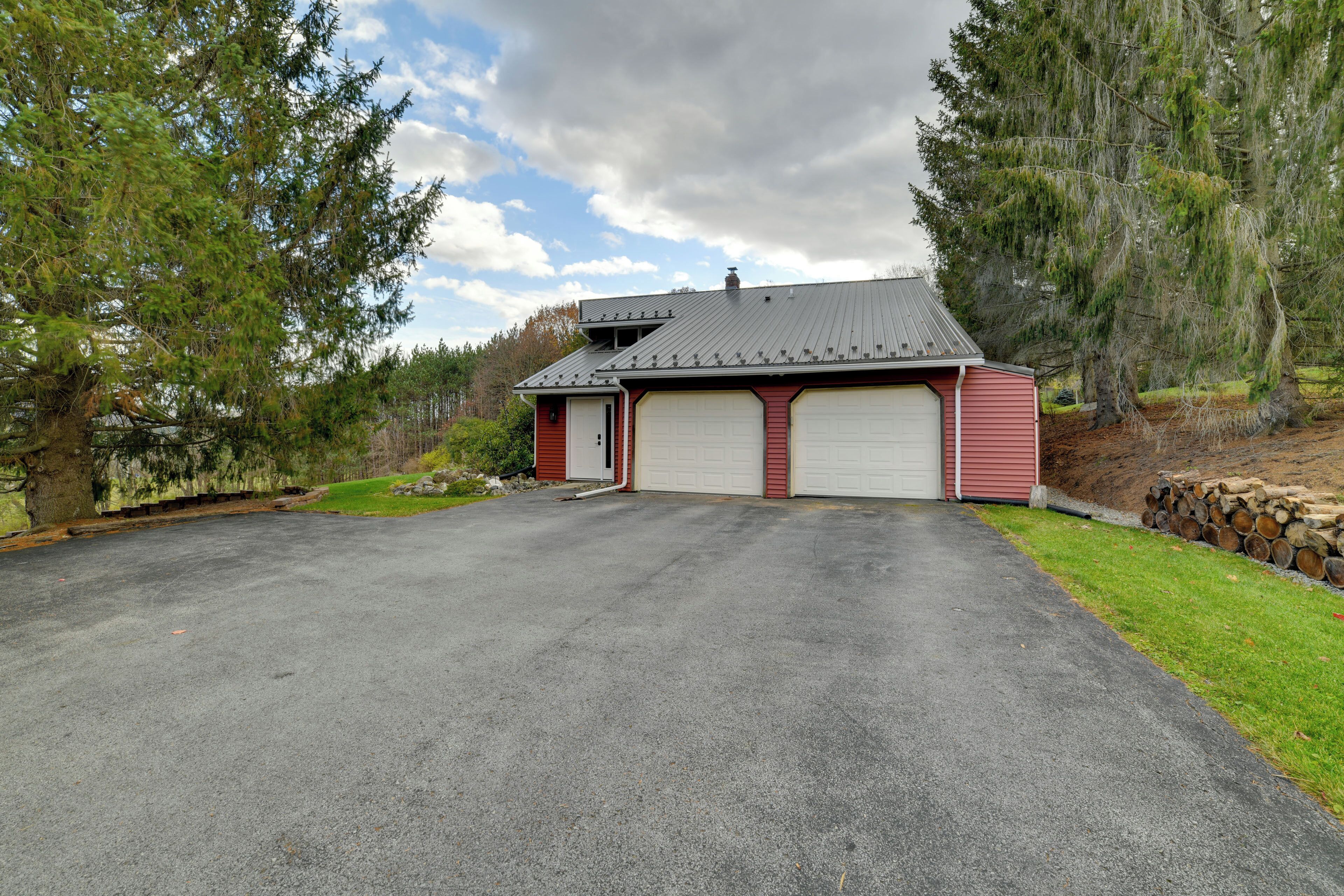 Une maison à deux étages avec un garage, entourée d’arbres et d’une pelouse bien entretenue.