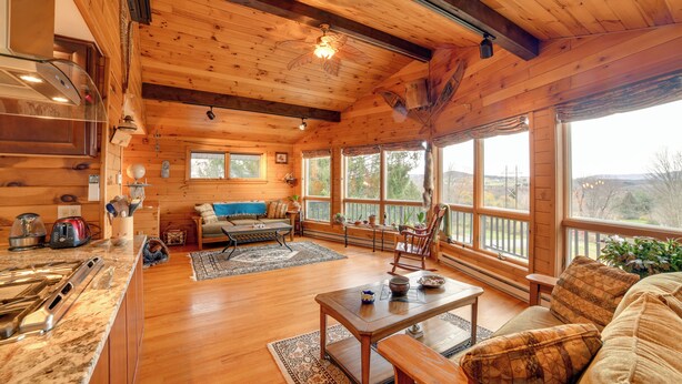 A spacious cabin with a wooden interior, a dining area, and large windows offering views of the outdoors. - Spacious Finger Lakes Home w/ Mountain Views (Dryden)