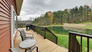 A deck with outdoor furniture, a pond, and a forested area. - Spacious Finger Lakes Home w/ Mountain Views (Dryden)