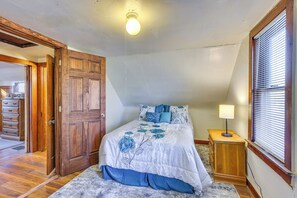 Ein Schlafzimmer mit Holztür, einem Bett mit Blumenmuster-Bettwäsche, einem Nachttisch mit Lampe und einem Fenster mit Jalousien.