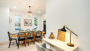 A dining area with a wooden table, black chairs, a vase, and a desk with a lamp.