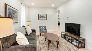 A modern living room with a sofa, armchair, coffee table, TV stand, and a large flat-screen TV.