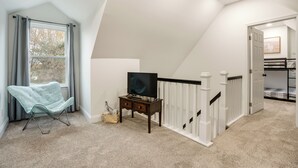 A bedroom with a bed, a TV on a stand, a window with curtains, and a staircase.
