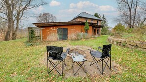 A house with a brick exterior and a metal roof, surrounded by a grassy yard with two black folding chairs and a small fire pit. - Historic Wisconsin Retreat on 26-acre Property! (Plain)