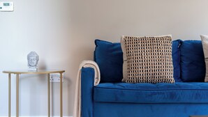A room with a blue sofa, a small round table with a Buddha statue, and a wall-mounted thermostat. - The Lewisham Collection (London)