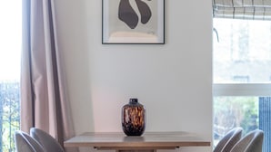 A dining area with a wooden table, four grey chairs, a vase, and a framed abstract artwork on the wall. - The Lewisham Collection (London)