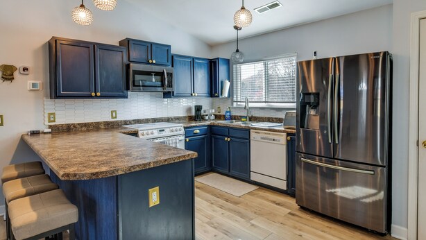 A modern kitchen with dark blue cabinets, a stainless steel refrigerator, a built-in oven, and a granite countertop.
